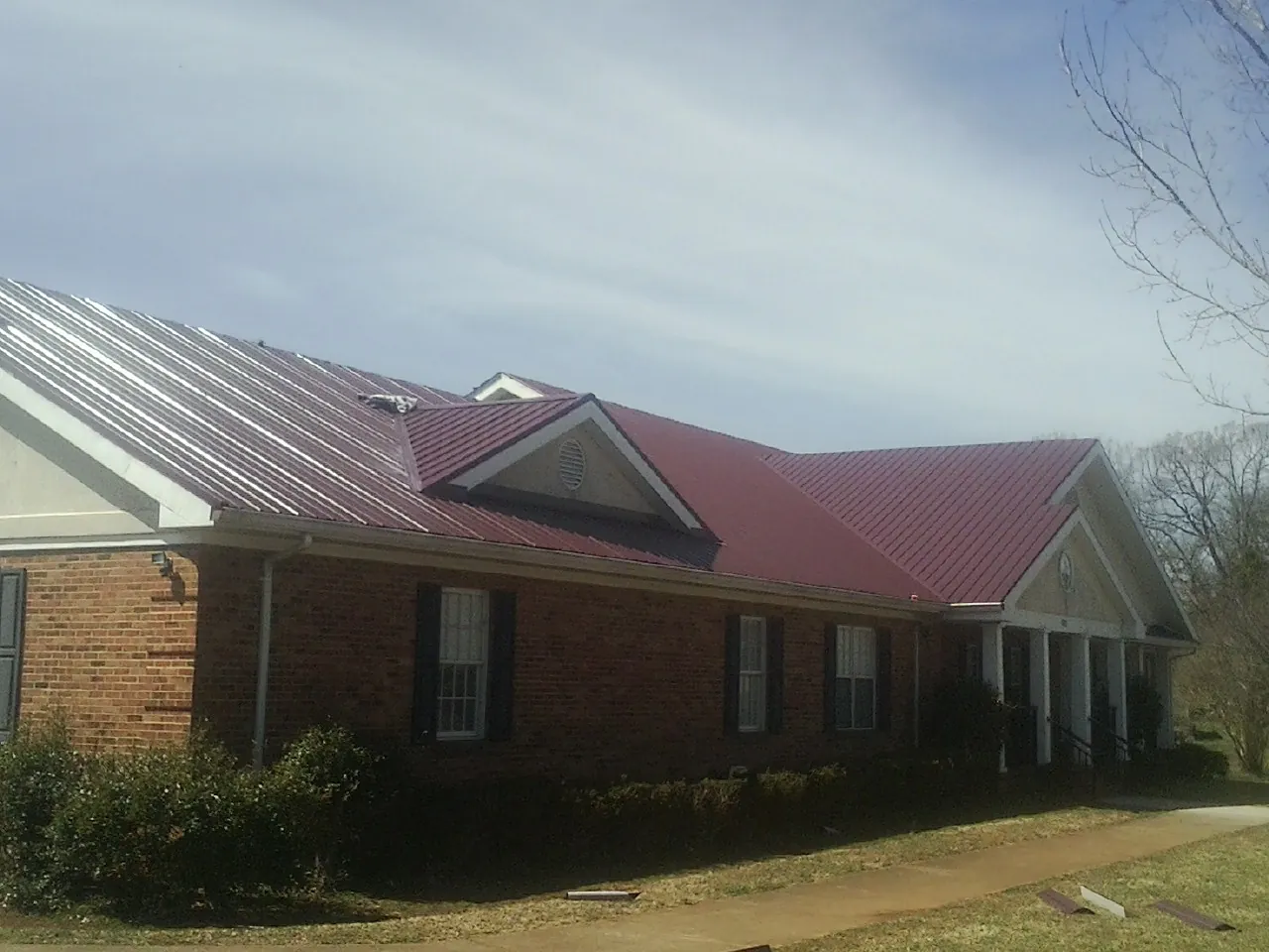 Red metal roof with gabled entries on a long brick building, from a Hail Damage Roof Repair job in Upland