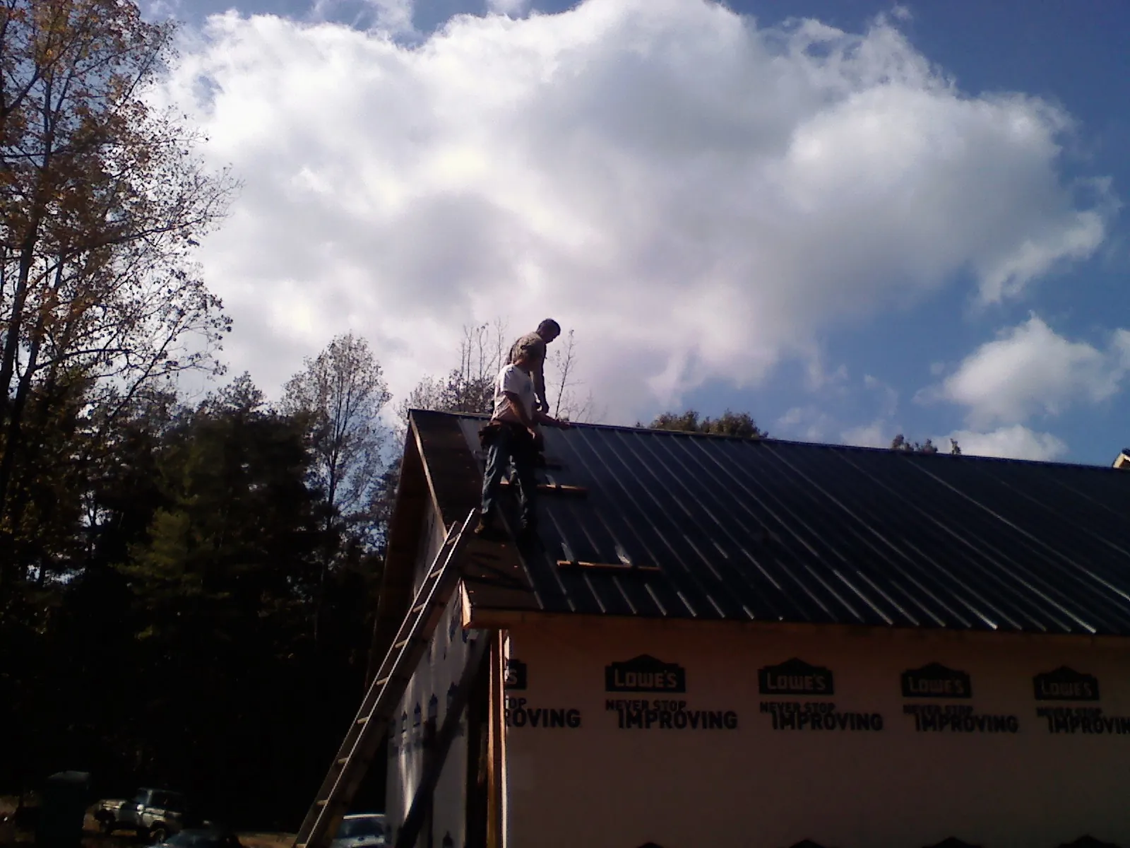 Roofer fastening dark metal panels high against a cloudy sky, from a Roof Inspection job in Upland