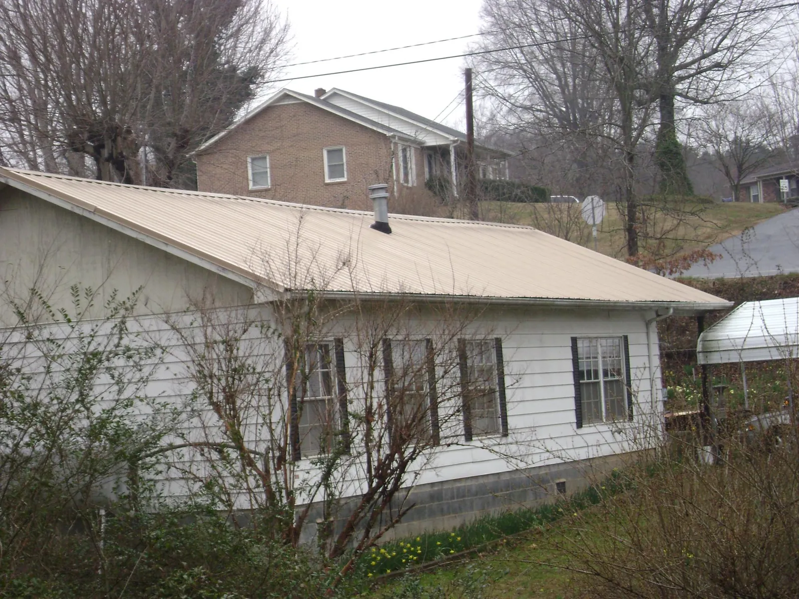 Tan metal roof on a white sided house set into a hillside — Commercial Roofing by Roofing Brothers in Upland